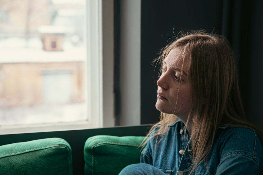 A cute young woman is sitting on the sofa by the window.