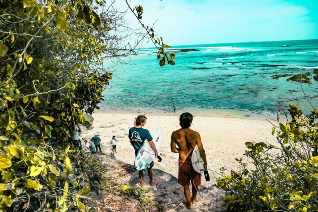 a couple of boys walking on a beach with water and trees